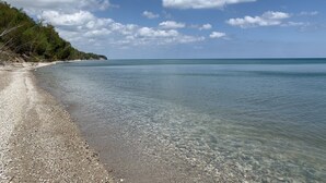 Une plage de sable clair parsemée de galets, avec une mer calme sous un ciel bleu nuageux.
