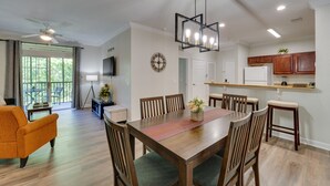 Ein Essbereich mit einem Holztisch, Stühlen und einer modernen Deckenleuchte. Es gibt eine Küchenzeile mit Holzschränken und einem Kühlschrank.