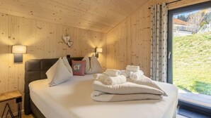 A wooden-paneled bedroom with a bed, pillows, a nightstand, and two wall-mounted lamps.