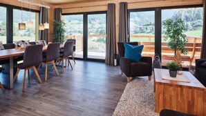A spacious room with a wooden ceiling, large windows, a dining area with a table and chairs, and a seating area with a sofa and a small table.