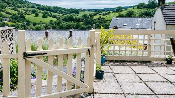 A gated terrace with a view of a green landscape and a building with a sloped roof. - Painter`s Cottage, a charming cottage in historic Town of Matlock Bath (Derbyshire)