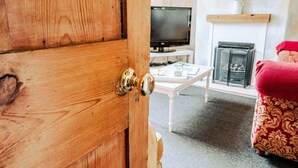 A wooden door with a brass handle, a television on a stand, a white table, and a patterned ottoman. - Painter`s Cottage, a charming cottage in historic Town of Matlock Bath (Derbyshire)