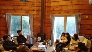A cozy cabin interior with wooden walls, a fireplace, and large windows. - Loghouse kizuki (Tsuru)