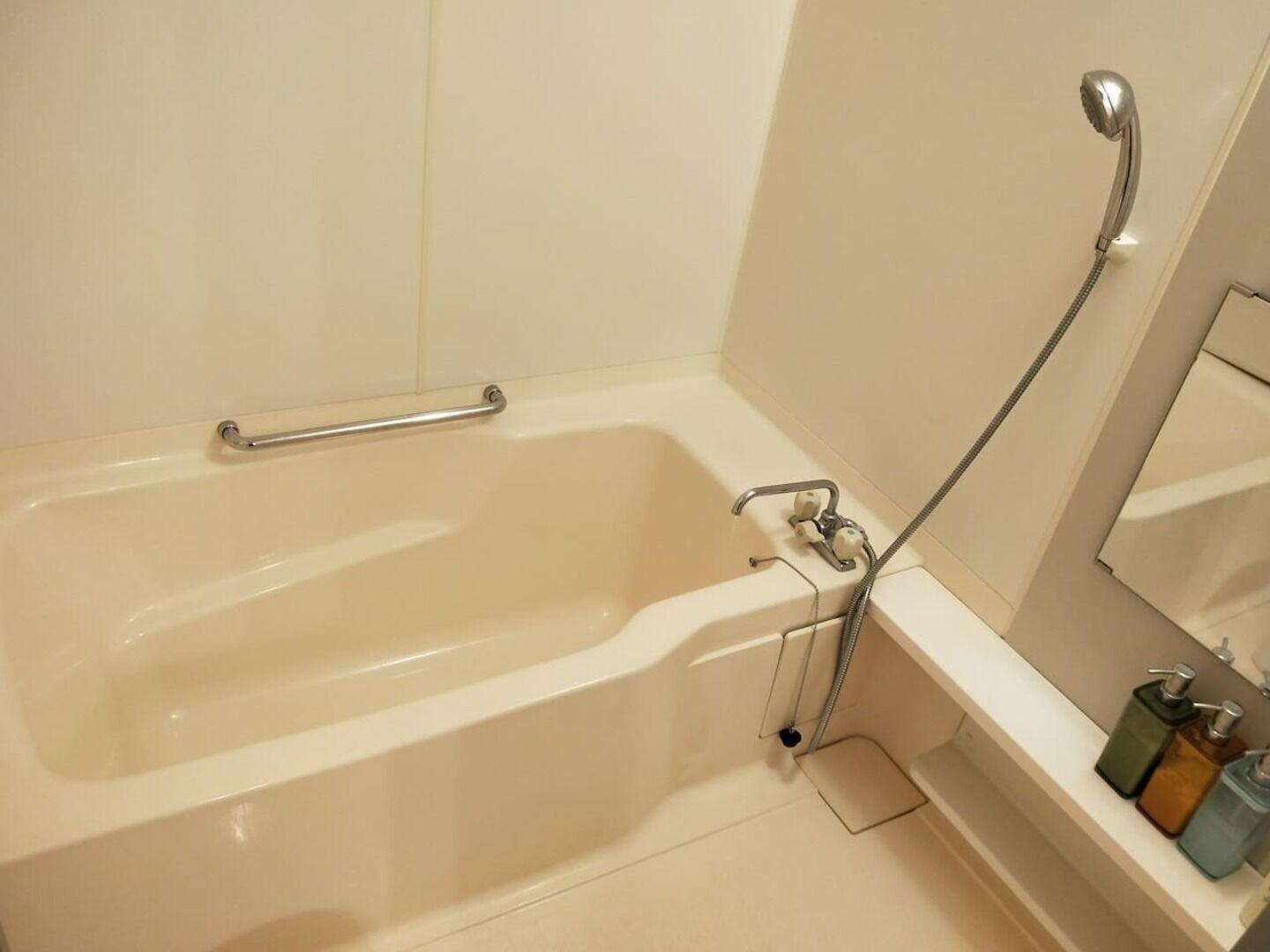 A bathtub with a handheld showerhead, a grab bar, and a shelf with toiletries.