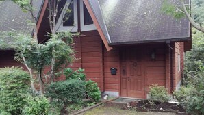 A wooden house with a steeply pitched roof, a front door, and a small porch area. - Loghouse kizuki (Tsuru)