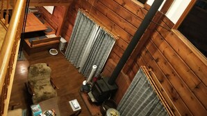 A cozy cabin interior with a wooden interior, a fireplace, a sofa, a dining table, and curtains. - Loghouse kizuki (Tsuru)
