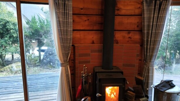 A cozy cabin with a wood-burning stove, large windows, and a view of the outdoors. - Loghouse kizuki (Tsuru)