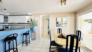 Une cuisine moderne avec des meubles blancs, un plan de travail bleu et un coin repas comprenant une table en bois et des chaises noires.