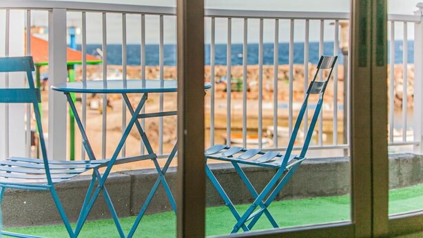 Un balcón con una mesa y dos sillas, con vistas a la playa.