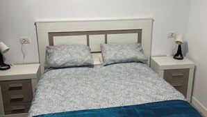 Un dormitorio con una cama, dos mesitas de noche y una lámpara fijada a la pared.