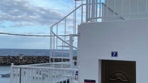 Un edificio costero con fachada blanca, una puerta marrón y una escalera que lleva a un balcón.