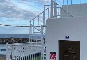 Un edificio costero con fachada blanca, una puerta marrón y una escalera que lleva a un balcón.