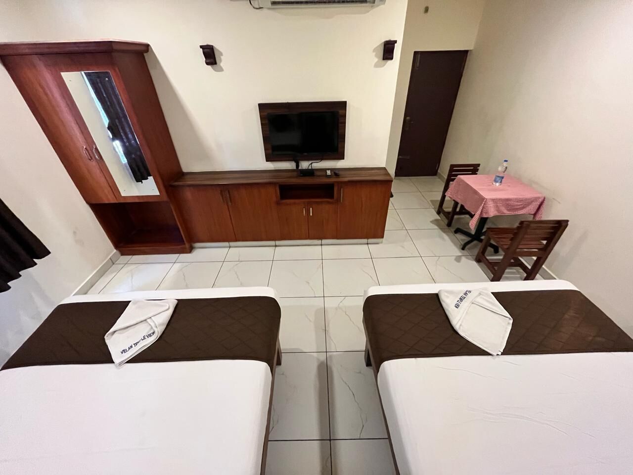 A hotel room with two beds, a TV, a small table with a pink tablecloth, and a wooden cabinet.