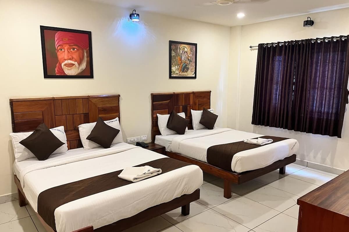 A hotel room with two beds, each with a wooden headboard, white bedding, and dark brown throw pillows. There are two wall-mounted light fixtures, a window with dark curtains, and a ceiling fan.