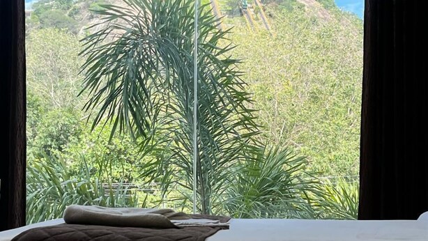 A bed with a view of a lush green landscape and a railway track. - Velan Temple View (Palani)