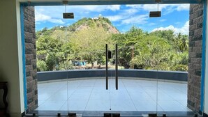 A room with a checkered table, a view of a mountain, and a glass door leading outside. - Velan Temple View (Palani)