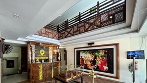 A reception area with a reception desk, a glass display case, a painting, and a staircase. - Velan Temple View (Palani)