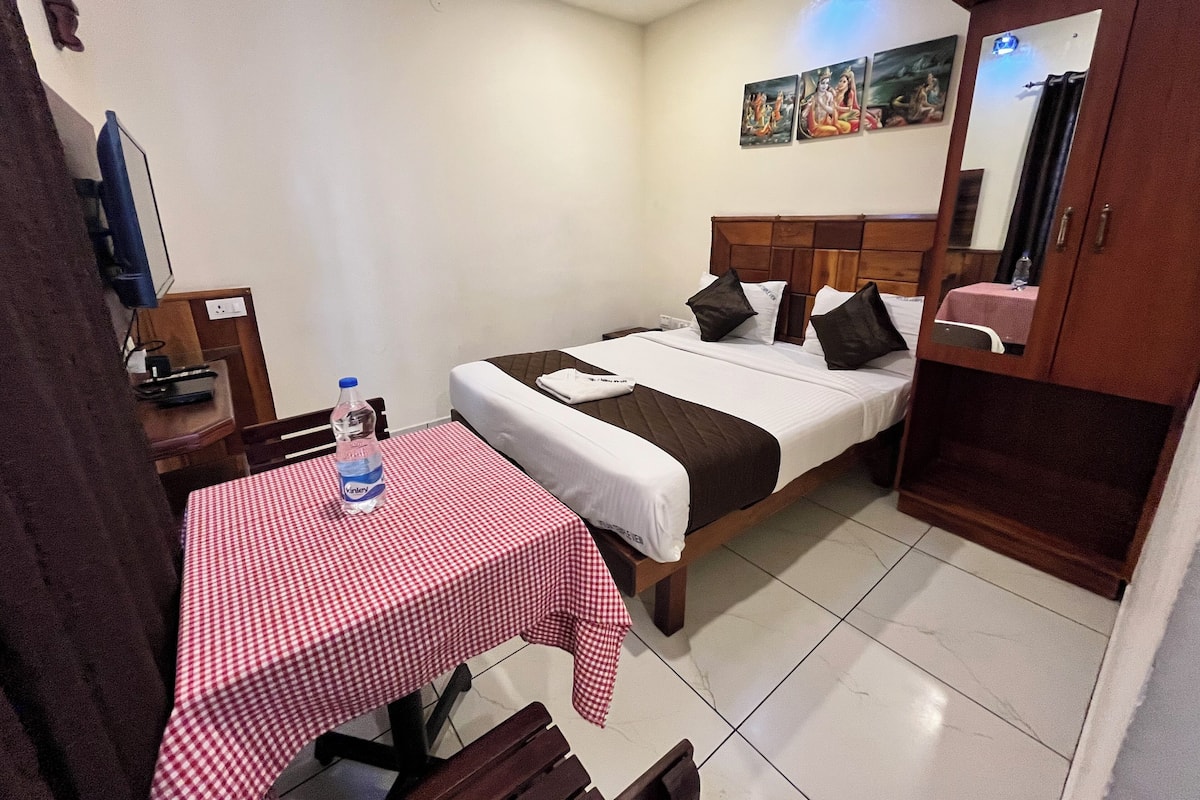 A hotel room with a single bed, a table with a checkered tablecloth, a bench, a water bottle, a TV, and a mirror.