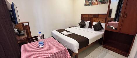 A hotel room with a single bed, a table with a checkered tablecloth, a bench, a water bottle, a TV, and a mirror.