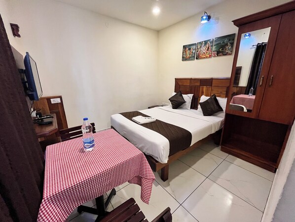 A hotel room with a single bed, a table with a checkered tablecloth, a bench, a water bottle, a TV, and a mirror.