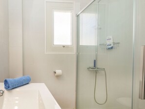Une salle de bain avec une douche à parois de verre, un lavabo blanc, une serviette et une fenêtre.
