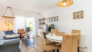 A modern living room with a sofa, dining table, wicker chairs, a TV, and a hanging light fixture. - Apartment Mirror by Interhome (Cunit)