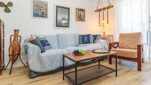 A living room with a striped sofa, a wooden coffee table, and a chair. There are framed pictures on the wall, a hanging light fixture, and a wooden floor. - Apartment Mirror by Interhome (Cunit)