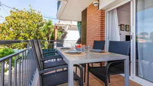 A balcony with a table set for two, wicker chairs, and a view of a building and trees. - Apartment Mirror by Interhome (Cunit)
