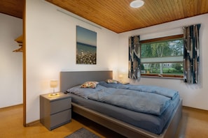 Une chambre à coucher comprenant un lit, des tables de chevet, une commode, une fenêtre avec des rideaux et un luminaire au plafond.