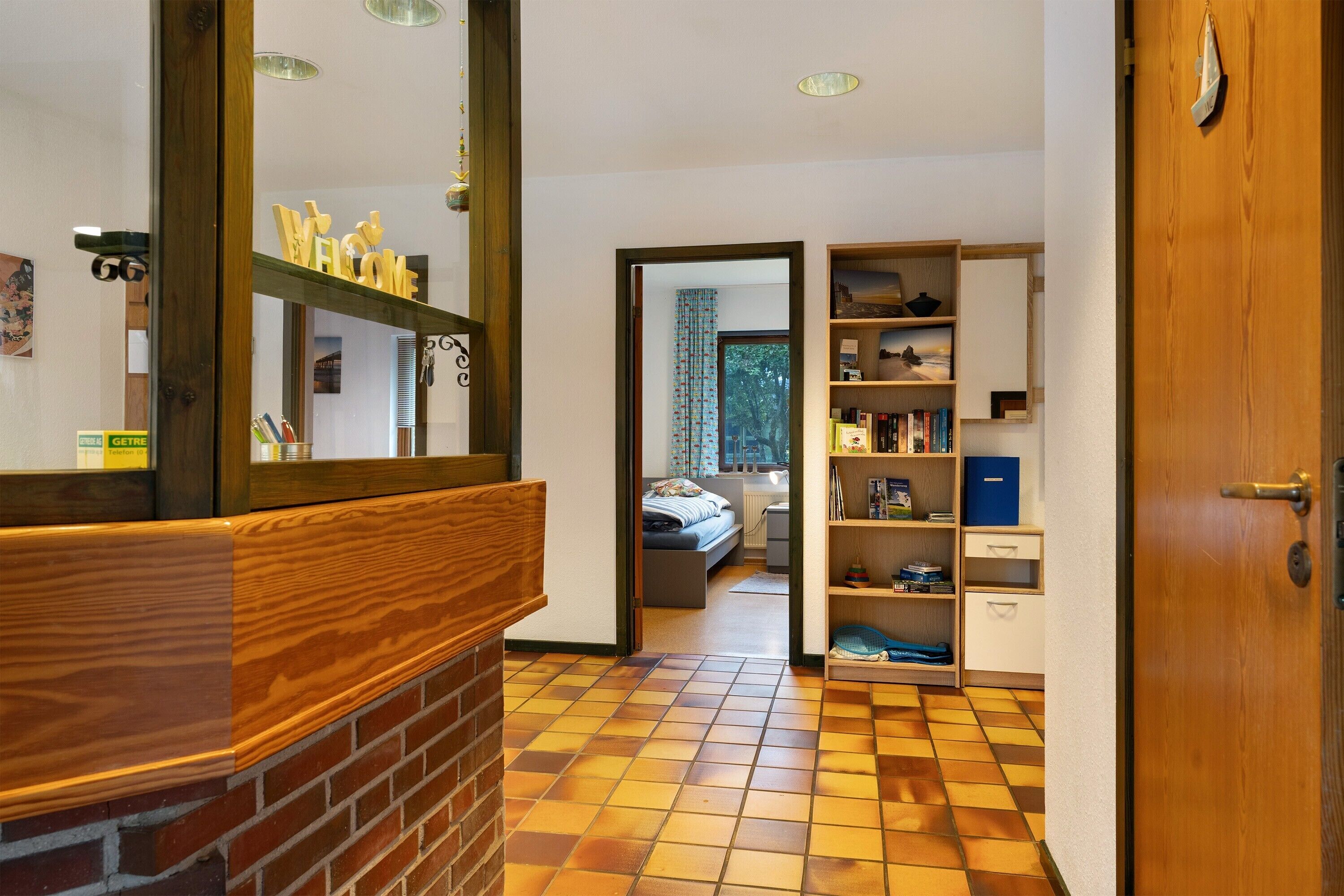 Un corridoio con una panca in legno, uno specchio, una libreria e una porta che conduce a una camera da letto.