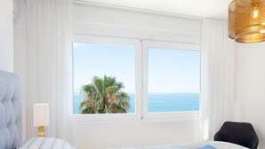A hotel room with a bed, a window with a view of the sea and palm trees, a lamp, and a chair. - Panorama Beach by Interhome (Torrox Costa)