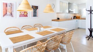 A modern kitchen with white cabinets, a wooden countertop, and a dining area with a white table and wicker chairs. - Panorama Beach by Interhome (Torrox Costa)