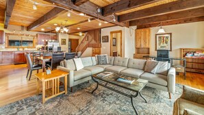 A spacious living room with a large sectional sofa, a wooden coffee table, and a dining area with a wooden table and chairs. A staircase with a wooden railing leads to an upper level. - Free EV Charger in 2 Car Garage-3 enSuites-EZ Walk to Resort/Free Town Bus-W/D in Unit-Dogs OK (Steamboat Springs)