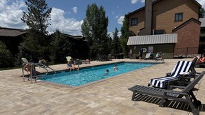 A swimming pool with lounge chairs and a brick building in the background. - Free EV Charger in 2 Car Garage-3 enSuites-EZ Walk to Resort/Free Town Bus-W/D in Unit-Dogs OK (Steamboat Springs)