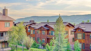 A row of log cabin-style buildings with multiple stories, surrounded by greenery and mountains in the background. - Free EV Charger in 2 Car Garage-3 enSuites-EZ Walk to Resort/Free Town Bus-W/D in Unit-Dogs OK (Steamboat Springs)