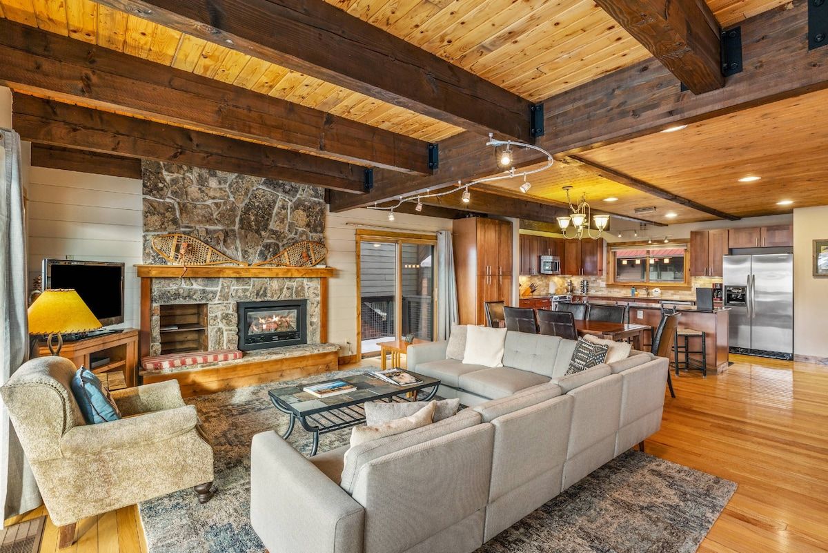 A spacious living area with a fireplace, a sofa set, and a kitchen in the background.