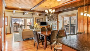 A spacious kitchen with a wooden ceiling, a dining area with a table and chairs, a television, and a stone fireplace. - Free EV Charger in 2 Car Garage-3 enSuites-EZ Walk to Resort/Free Town Bus-W/D in Unit-Dogs OK (Steamboat Springs)