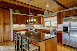 A modern kitchen with wooden cabinets, a central island, stainless steel appliances, and a window providing natural light. - FREE EV Charger-2 Car Garage-3 enSuites-W/D-DogsOK (Steamboat Springs)