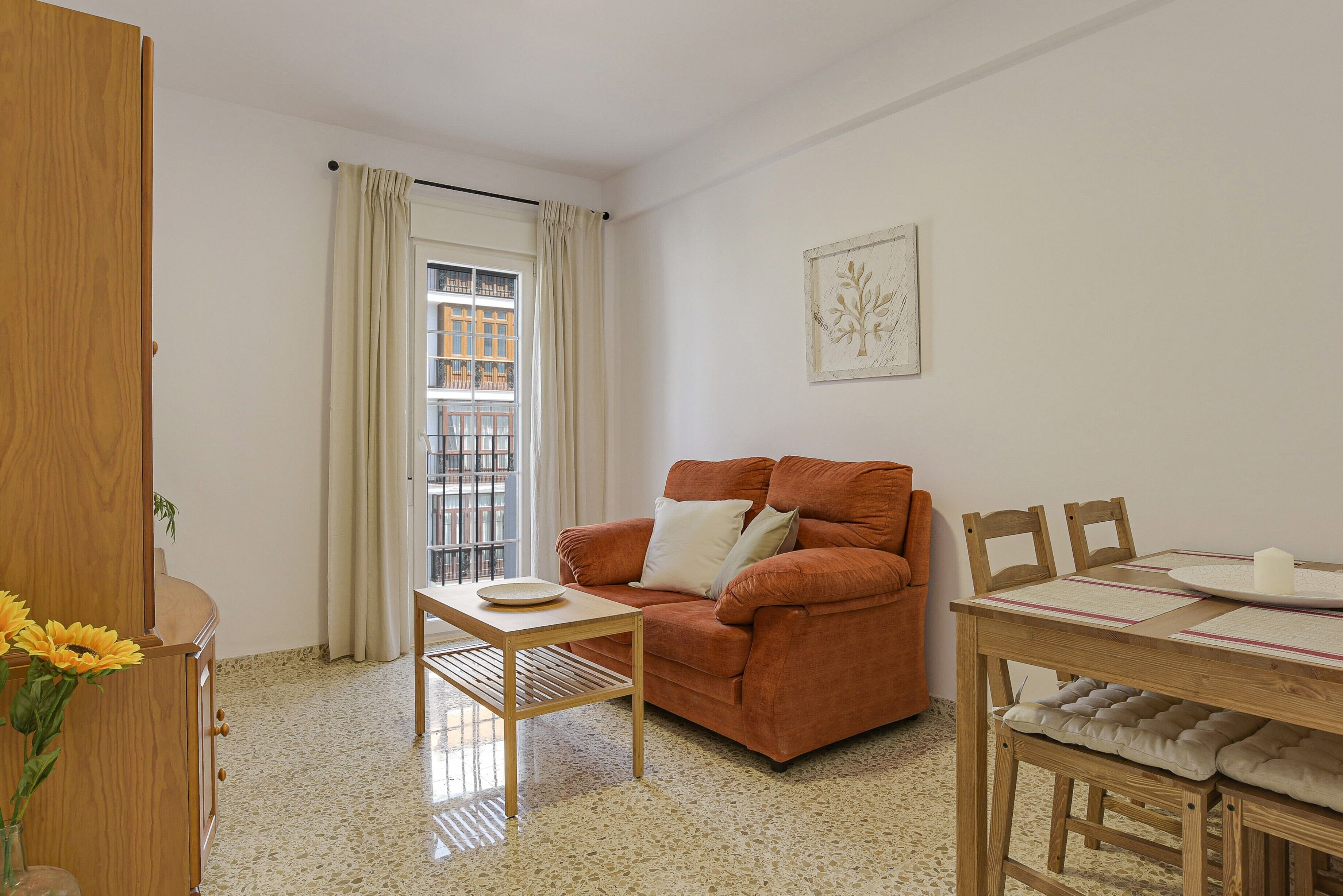 Uma sala de estar com sofá, mesa de jantar e janela com cortinas.