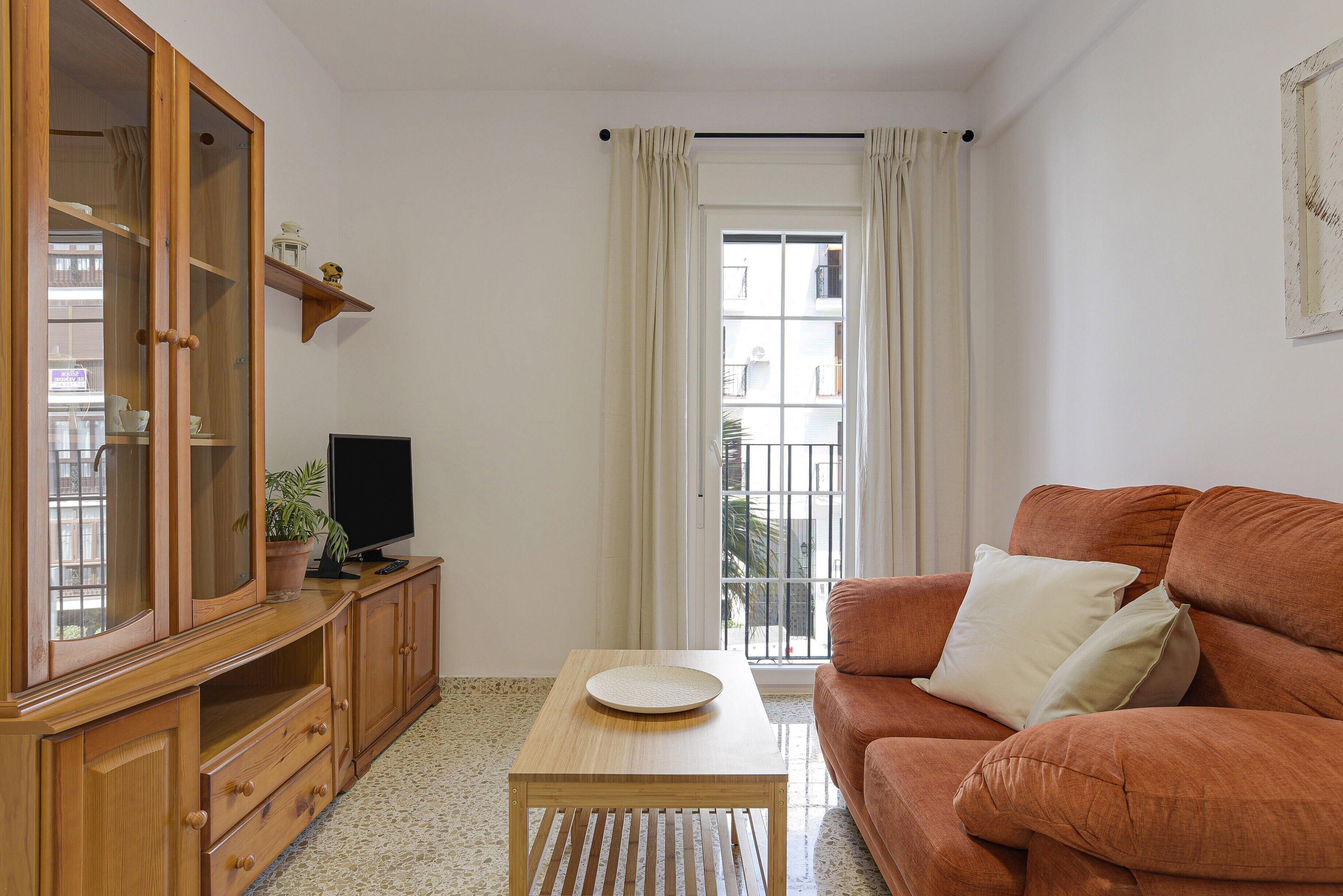 A living room with a wooden cabinet, a television, a sofa, and a window with curtains.