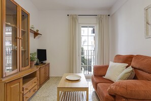 Ein Wohnzimmer mit Holzschrank, Fernseher, einer Couch und einem Fenster mit Vorhängen.