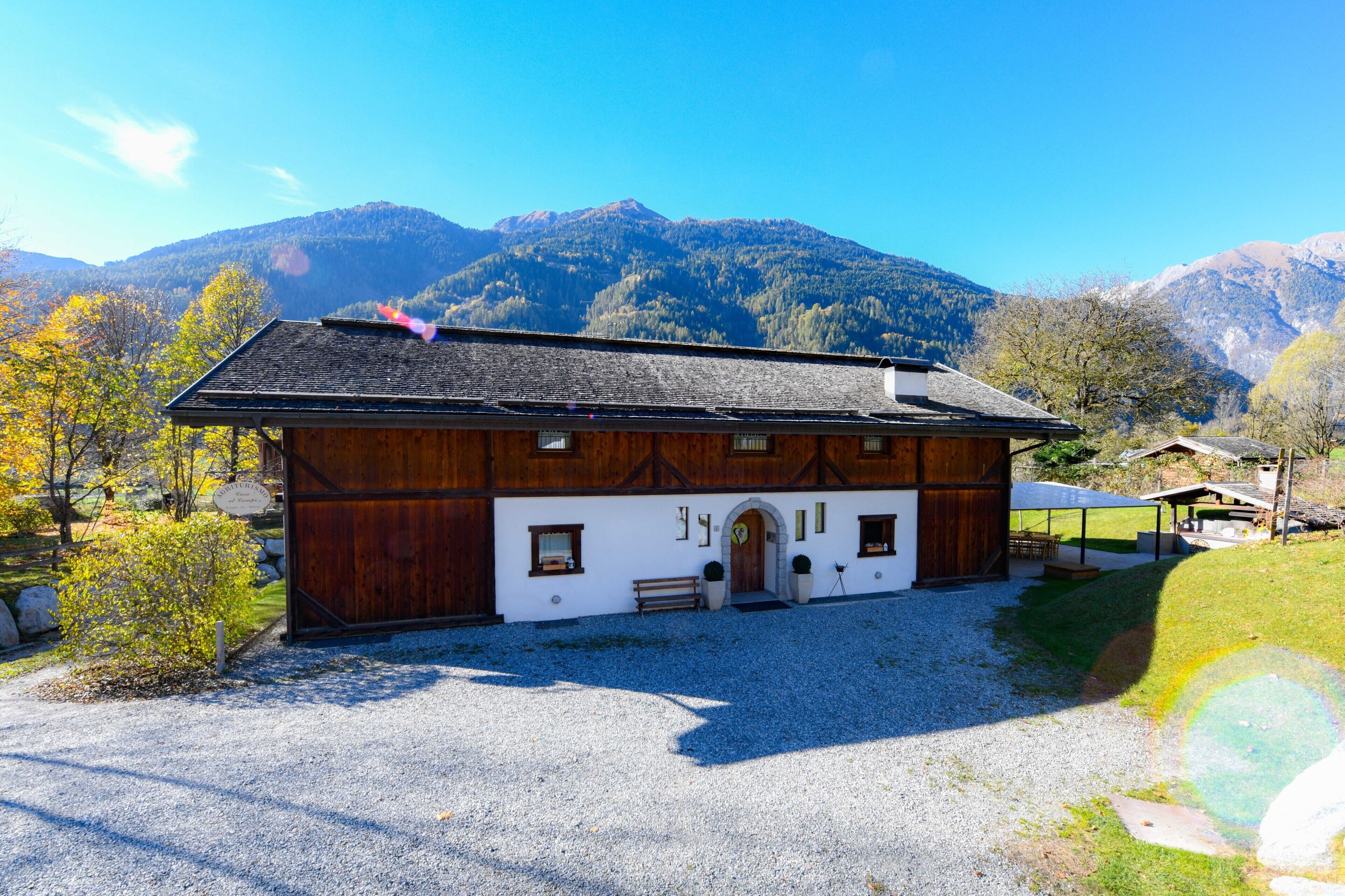 A wooden chalet with a gravel driveway, set against a mountainous backdrop.