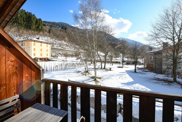 A wooden deck with a view of a snow-covered landscape, including a building with multiple windows and a mountain in the background.