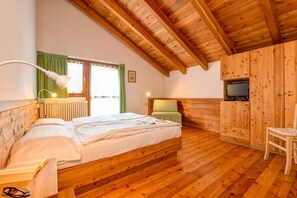 A wooden-paneled room with a bed, a chair, a desk, and a television.