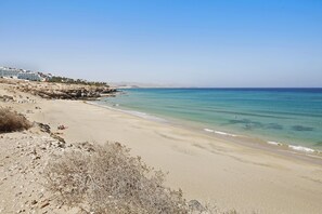 Une plage avec un rivage rocheux au premier plan, une étendue de sable et un ciel bleu dégagé.