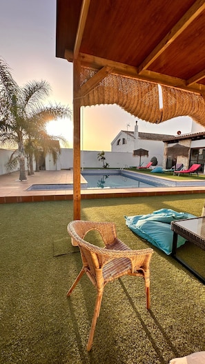 Un espacio al aire libre techado con piscina, sillones de descanso y una silla de mimbre.