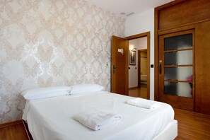 A neatly made bed with white linens, a wooden wardrobe with frosted glass panels, and a patterned wallpaper. - Chalet "Casa Juan Arias" Close to the Sea with Pool, A/C, Wi-Fi, Garden & Terrace (Conil de la Frontera)