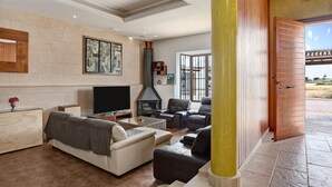 A living room with a fireplace, sofas, a TV, and a large window. - Chalet "Casa Juan Arias" Close to the Sea with Pool, A/C, Wi-Fi, Garden & Terrace (Conil de la Frontera)