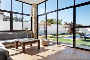 Una habitación soleada con un ventanal grande, un sofá, una mesa de centro y vistas a una piscina y jardín.