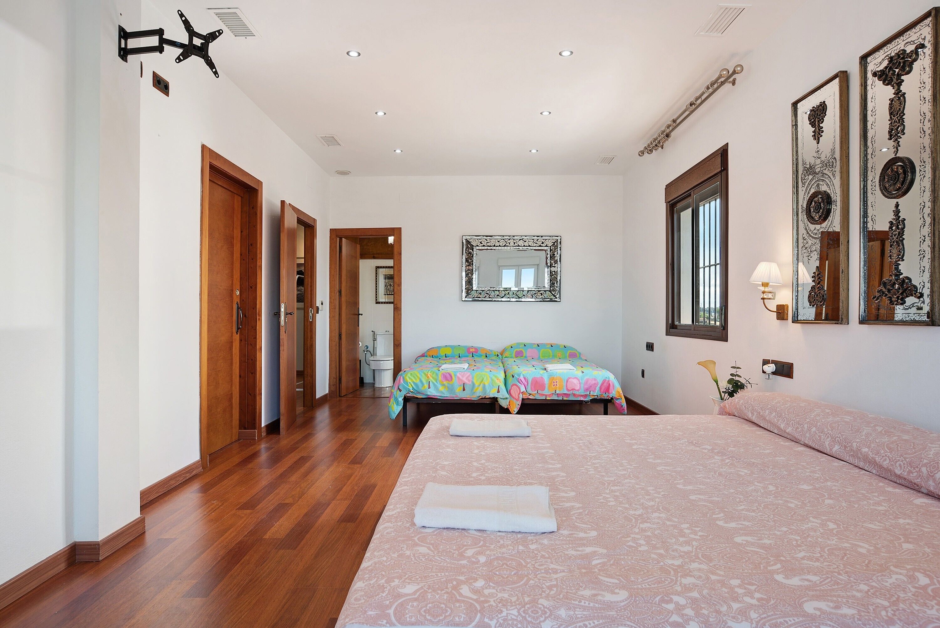 A bedroom with a large bed, a wooden floor, a mirror, and a window.
